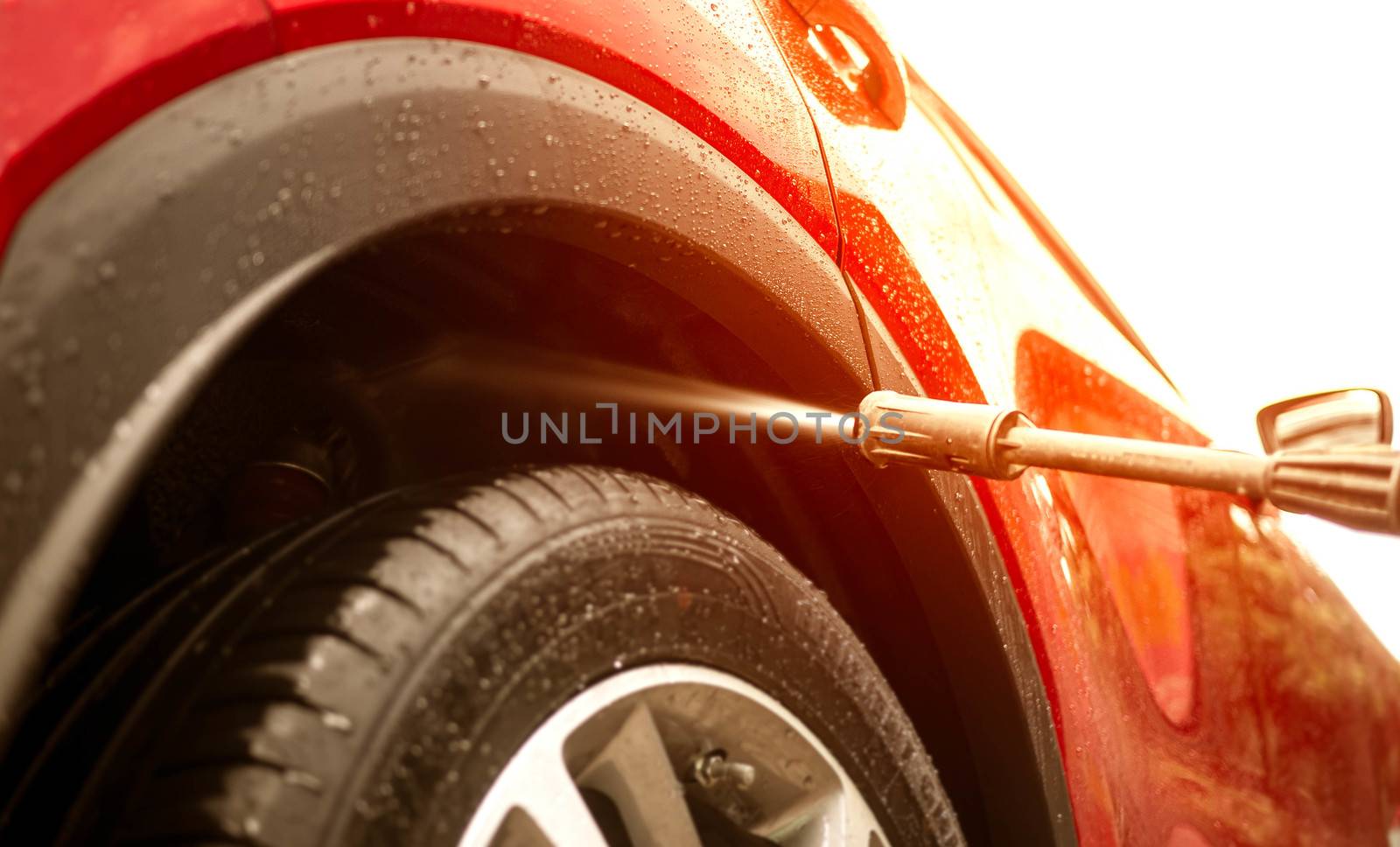Close-up of man holding a high-pressure water sprayer for washing car rear wheel fender.