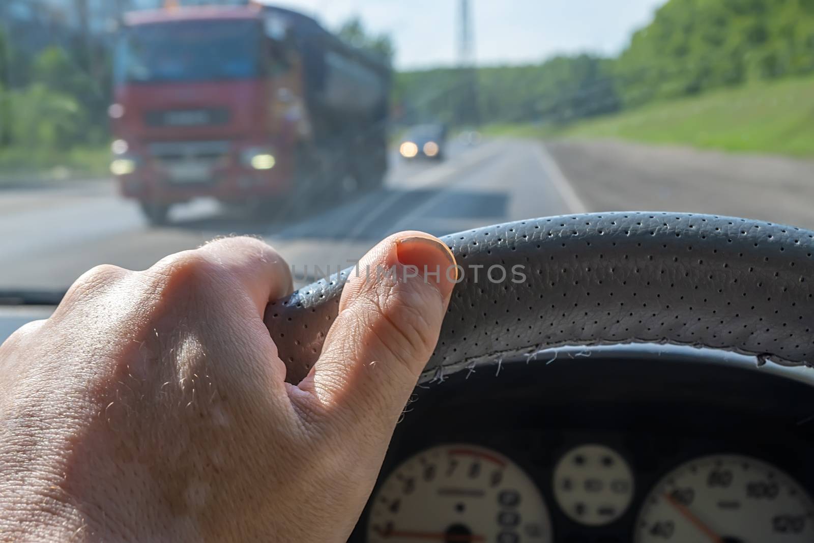 the driver's hand on the steering wheel in the car on the background of the road and passing towards the truck