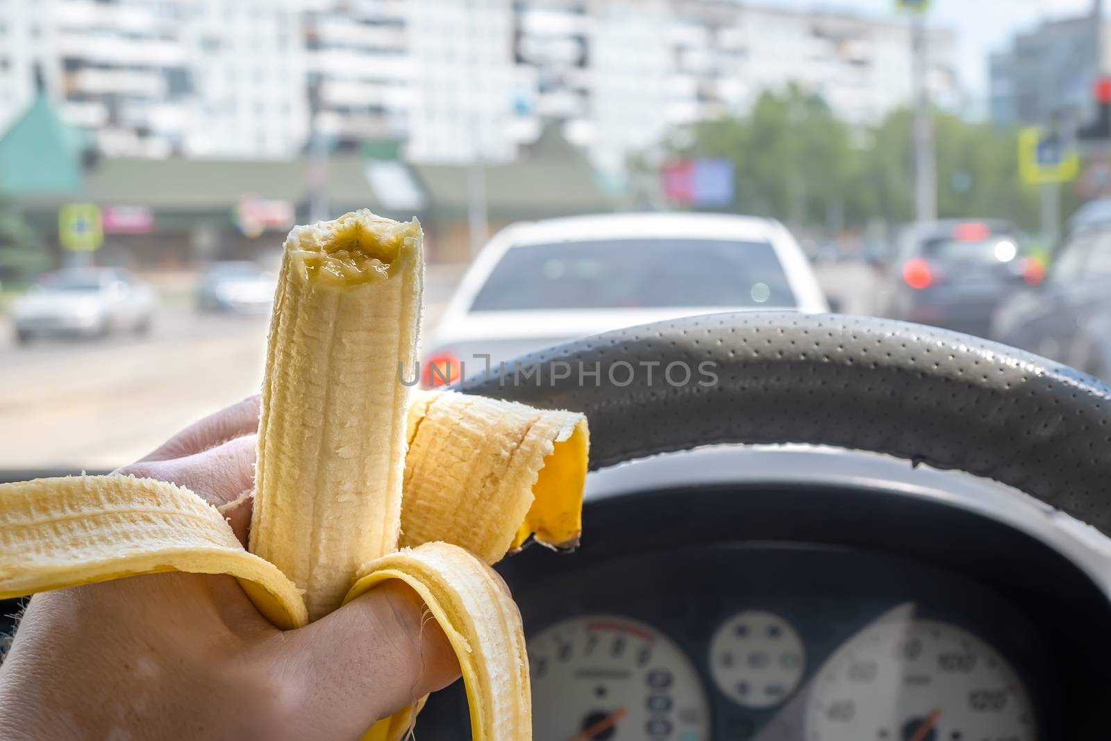 food, a bitten banana in the hand of a car driver who eats while driving on the roadway of the city