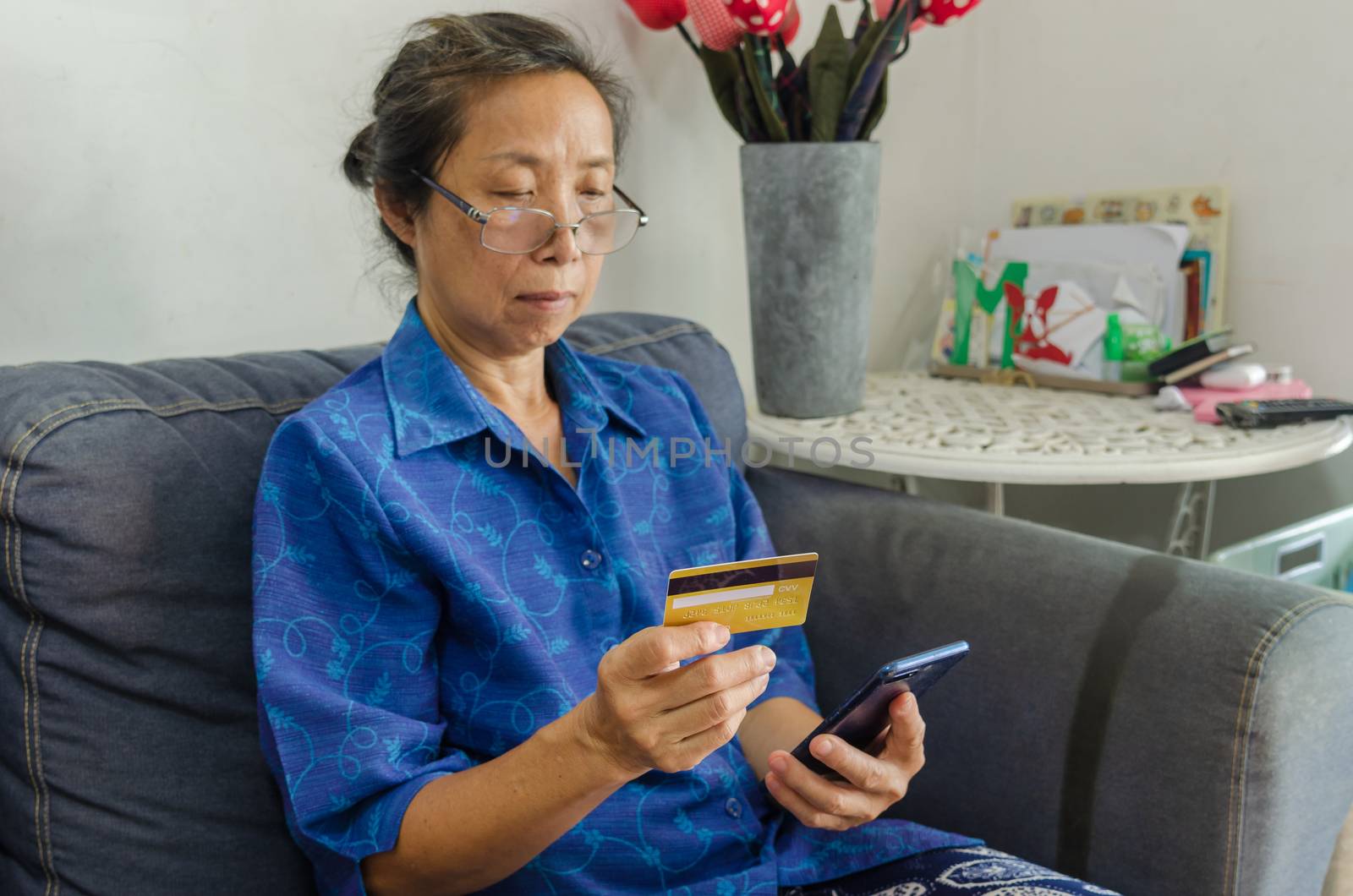 Portrait of a senior Asian woman holding mobile phone and credit cards shopping online.