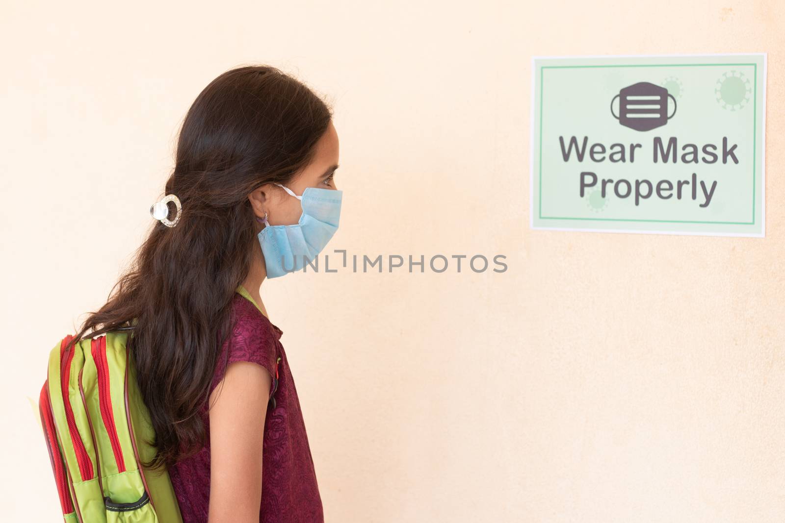 Young girl Student adjusting mask by seeing wear mask properly notice on classroom wall before entering class to protect from coronavirus or covid-19 infection. by lakshmiprasad.maski@gmai.com