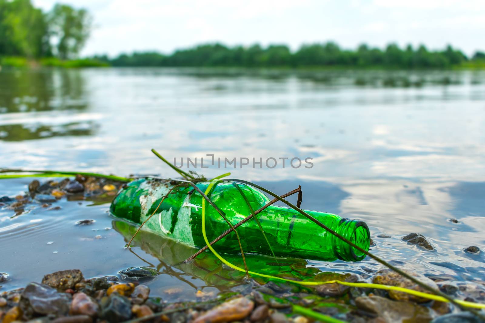 Glass bottle on the riverbank pollutes the environment. Nature pollution with garbage left by vacationers on the beach by Skaron