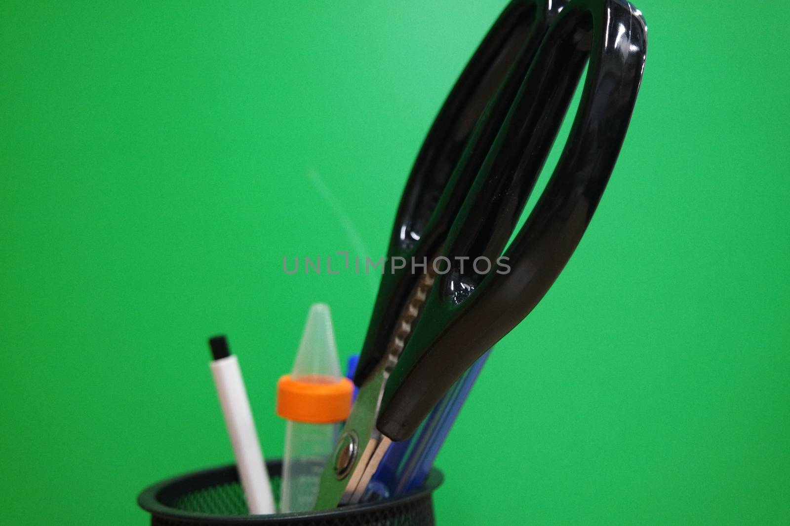 Closeup view of a stationery pot containing stationery items. stationery pot in front of a green background.