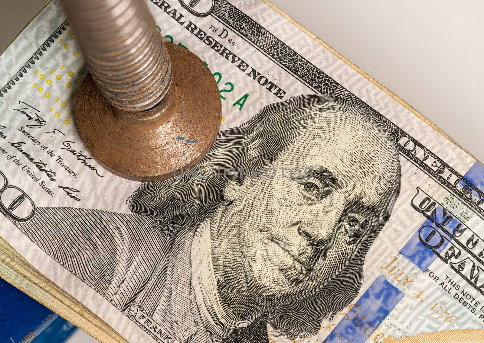 Concept for financial stress or recession. USA 100 dollar bills being squeezed between the jaws of a large vise or vice in detailed macro shot