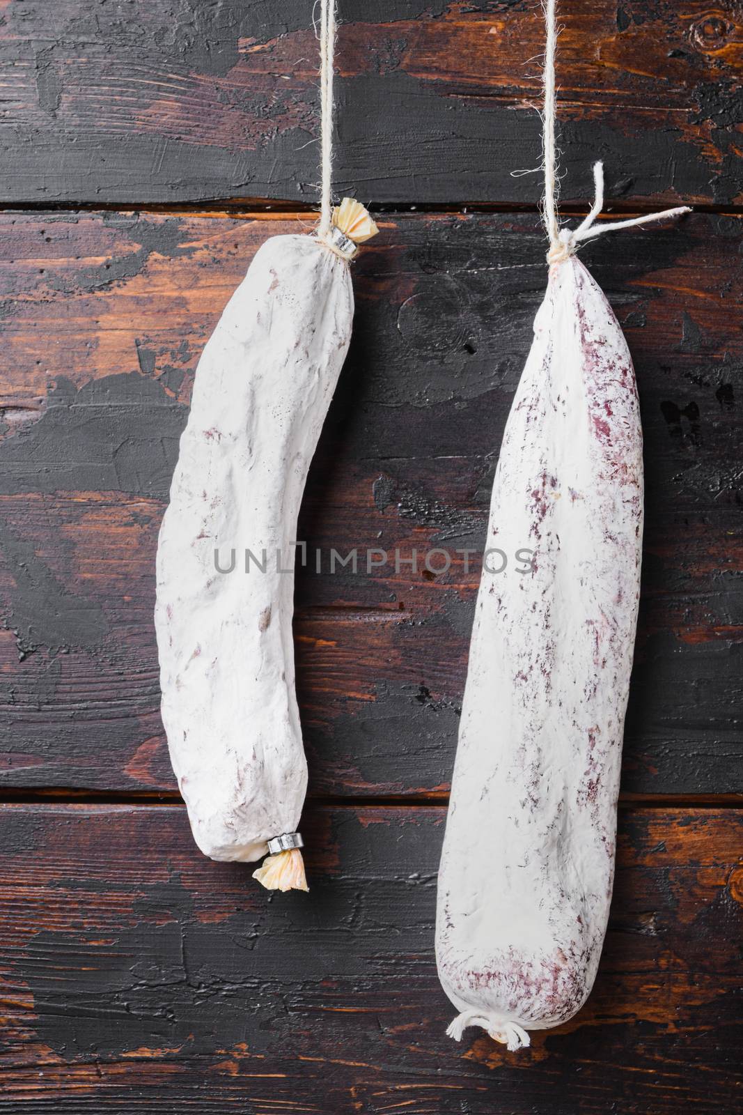 Spanish dry sausages hang from a rack at market on old wooden table.