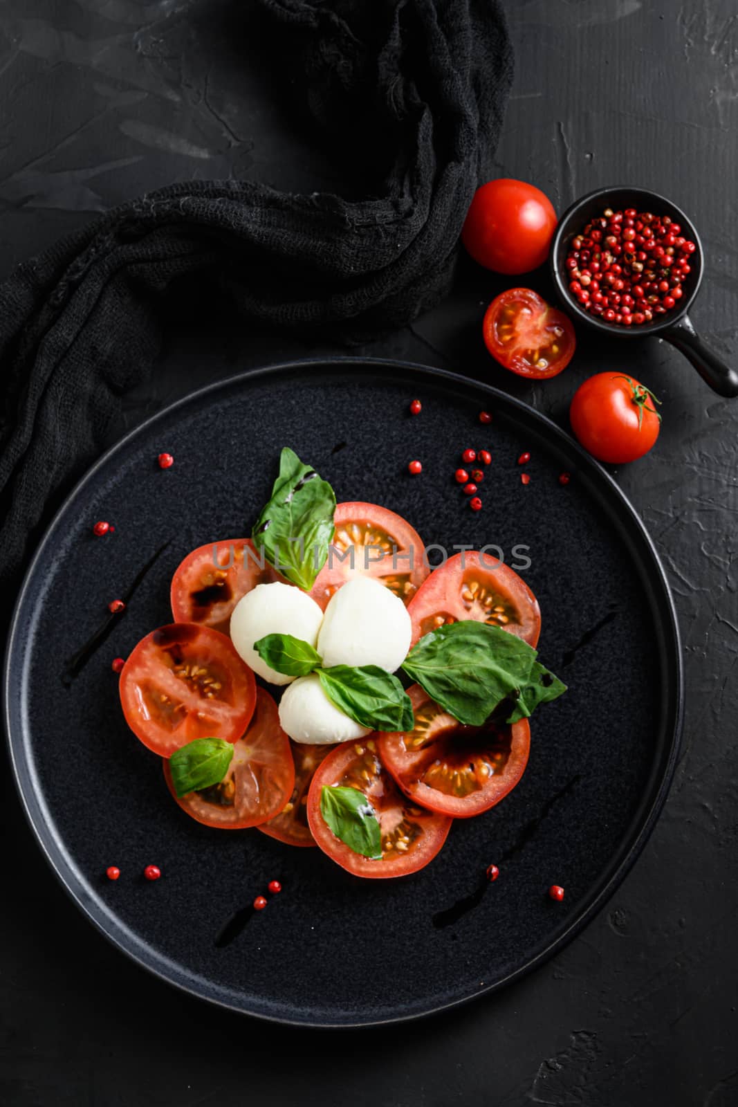 Caprese salad Italian cuisine concept Tomato and mozzarella slices with basil leaves on black ceramic platwantipasta black textured background top view by Ilianesolenyi
