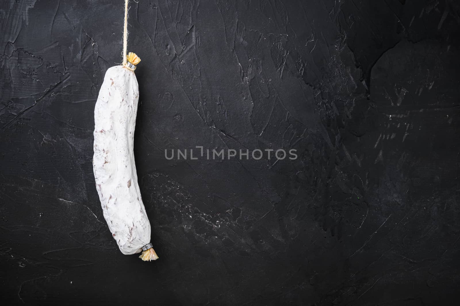 Spanish salchichon dry cured sausage on black background, topview with space for text.