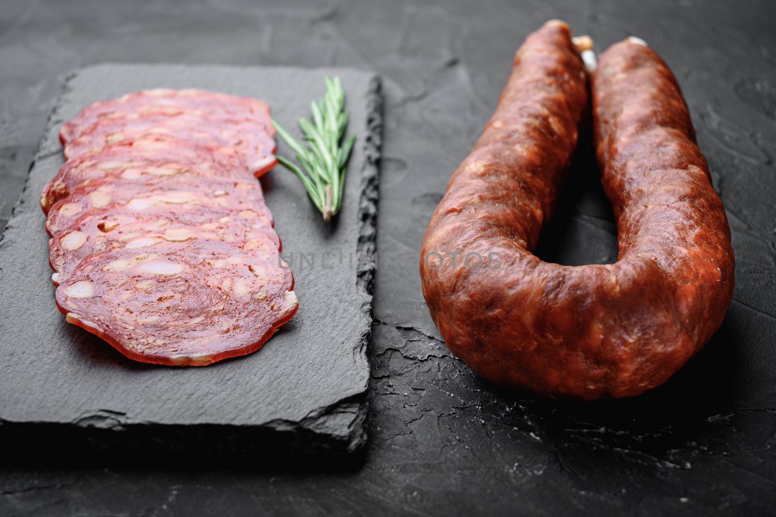 Whole and sliced chorizo sausage on black background.