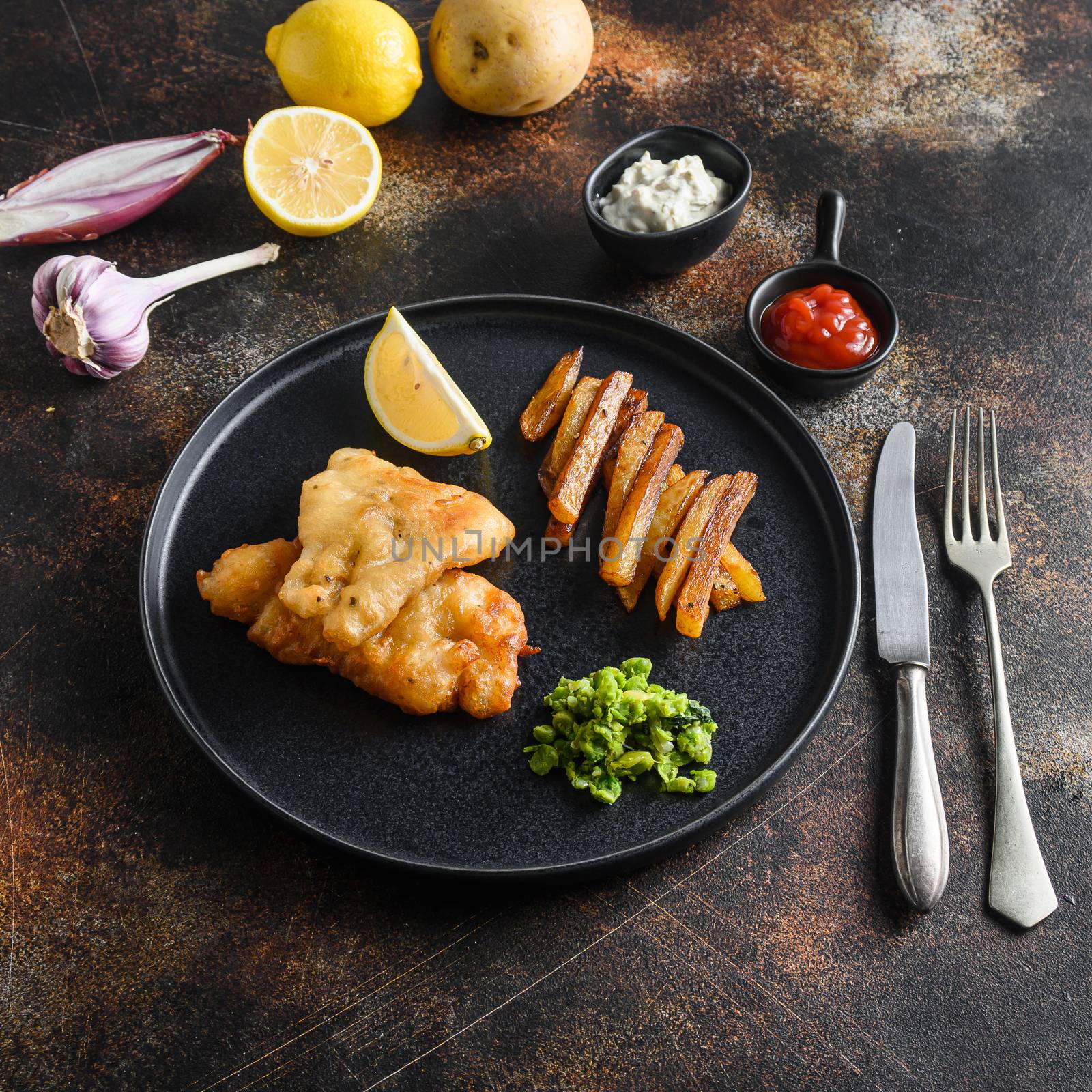 fish and chips with beer-battered cod and fries and a side of tartar sauce and mushy peas on black plate over old rustic metal style background top view square side view by Ilianesolenyi