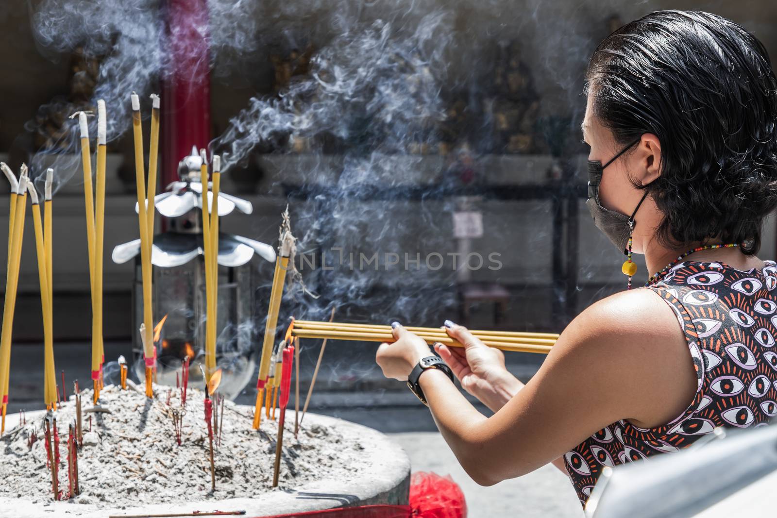 A young woman wearing face mask is burning incense in a Chinese  by tosirikul
