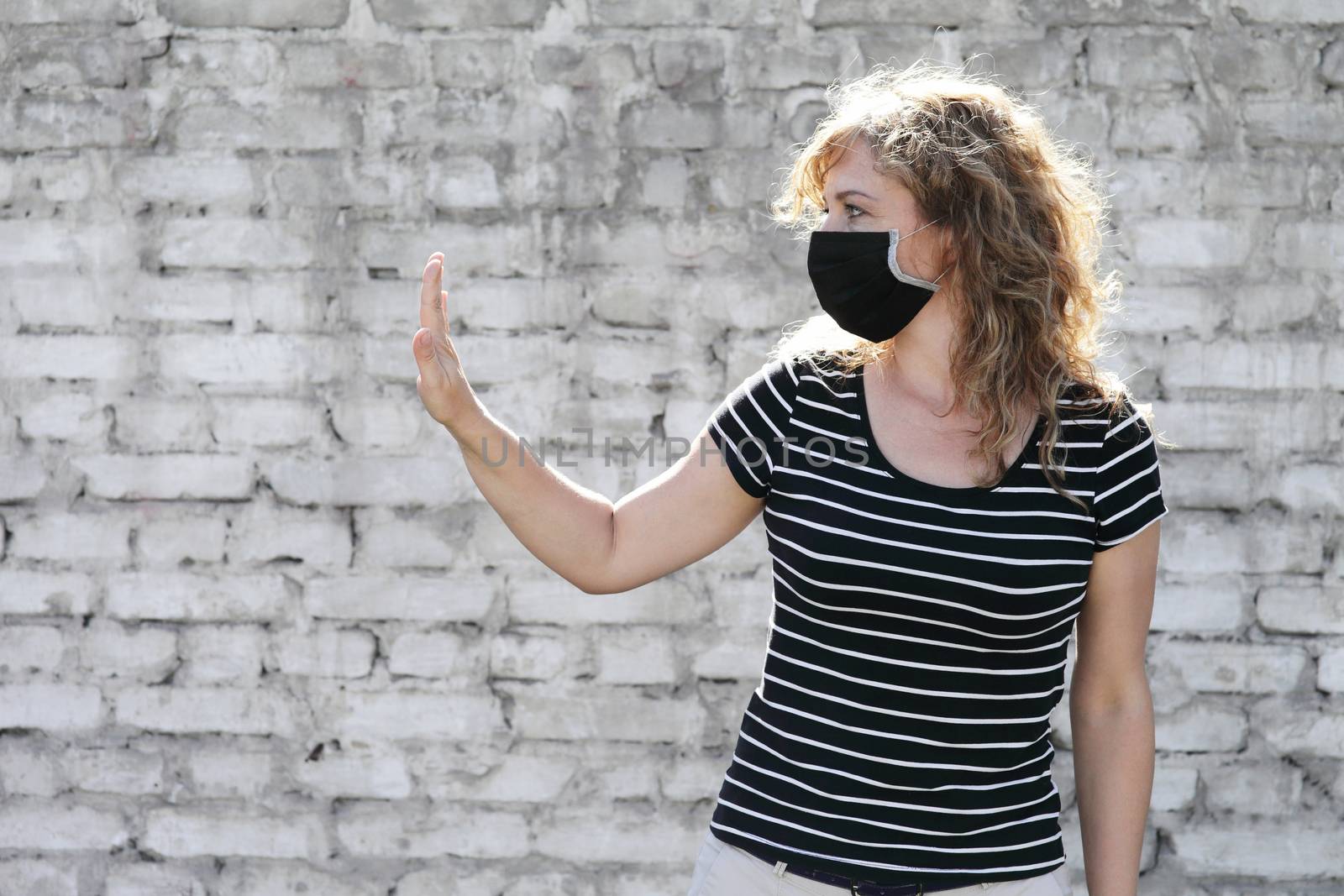 Portrait of a Girl in a protective mask free space for an inscription. Social distancing. White brick wall in the background. Shows stop by hand