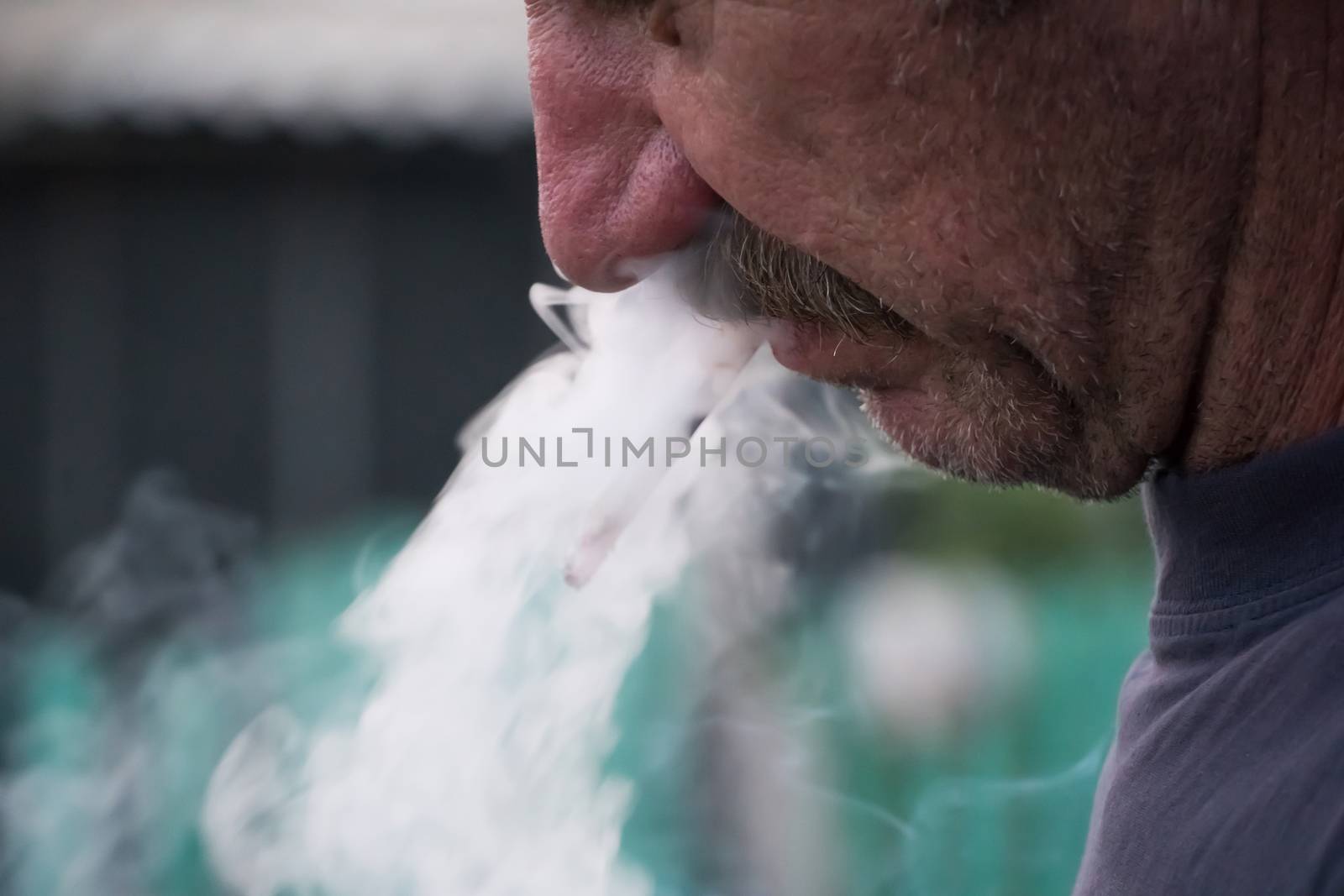 A man with a mustache smokes a cigarette in close-up. Thick smoke from tobacco Smoking and the concept of health. Nicotine addiction in humans.