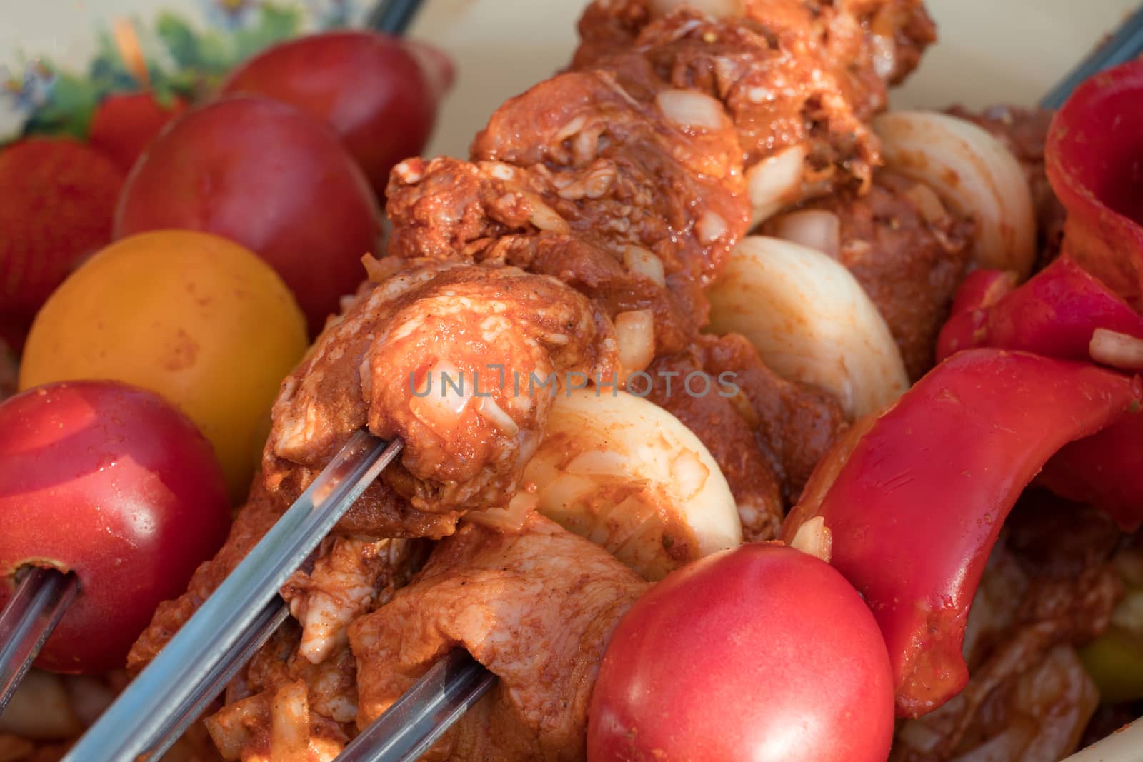 Marinated raw meat for shish kebab, barbecue or grill with onions, tomatoes and bell peppers on skewers. Cooking meat in the grill on skewers in nature in the summer on a picnic.