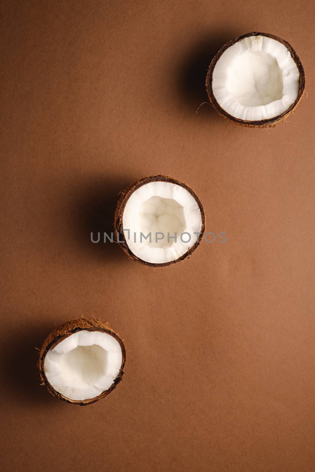 Three coconut fruits in row on brown plain background, abstract food tropical concept, top view