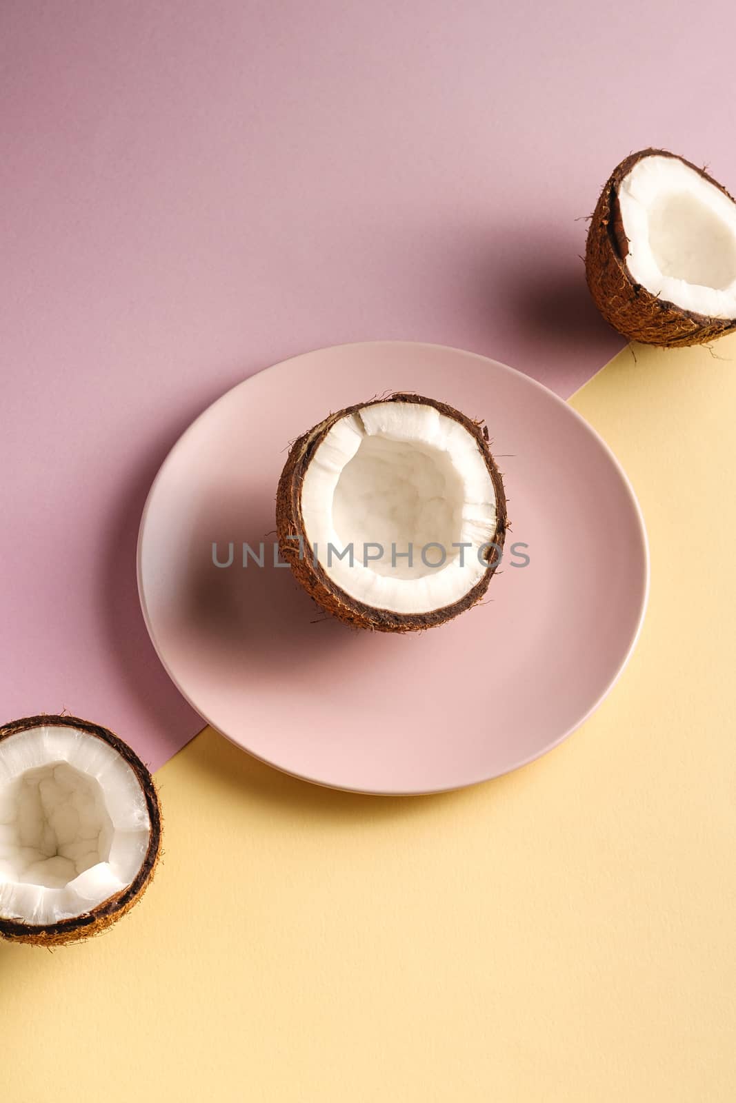 Coconut half in plate with nut fruits on cream yellow and pink plain background, abstract food tropical concept, angle view