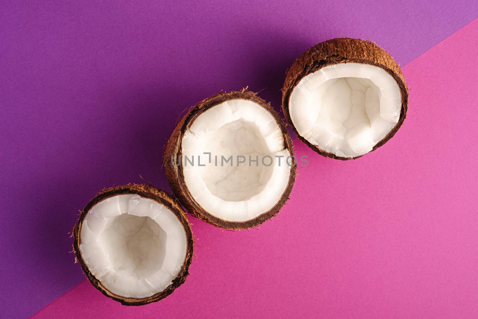 Coconut fruits in row on violet and purple plain background, abstract food tropical concept, top view