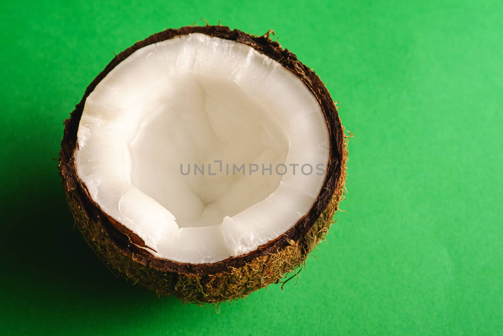 Single coconut fruit on green plain background, abstract food tropical concept, angle view macro