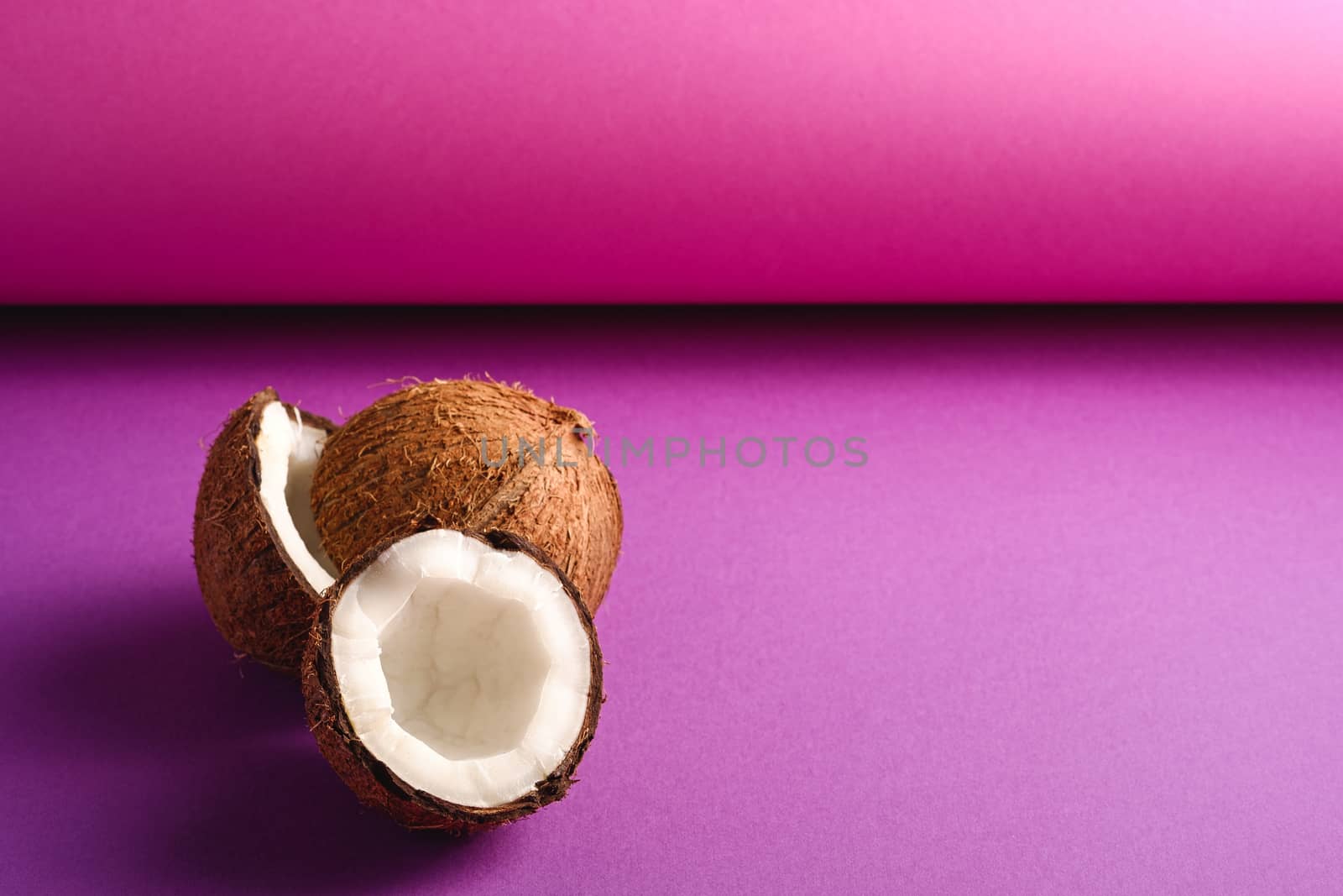 Coconut fruits on purple violet folded paper background, abstract food tropical concept, angle view copy space