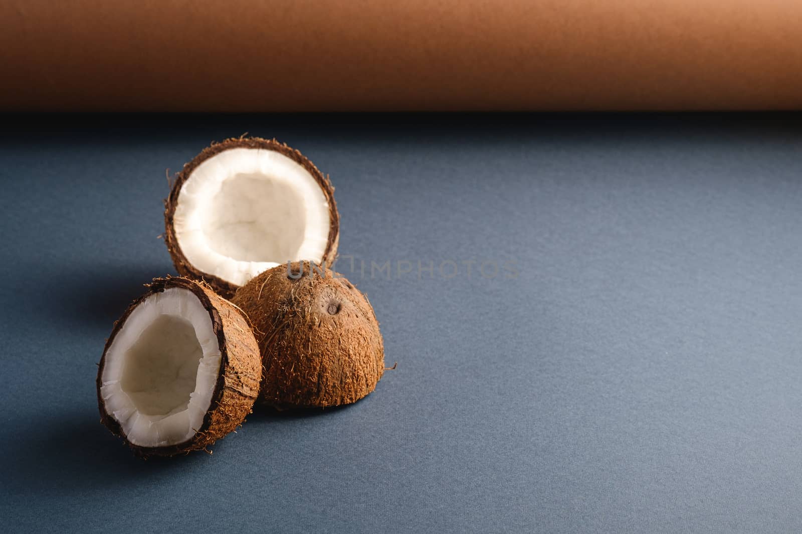 Coconut fruits on brown and blue grey folded paper background, abstract food tropical concept, angle view copy space
