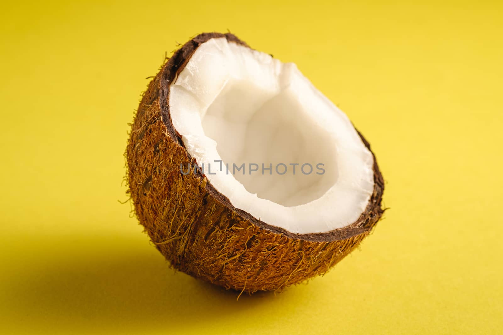 Single coconut fruit on yellow plain background, abstract food tropical concept, angle view macro