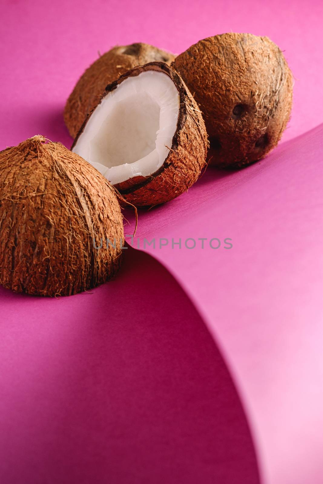 Coconut fruits on folded paper pink purple plain background, abstract food tropical concept, angle view