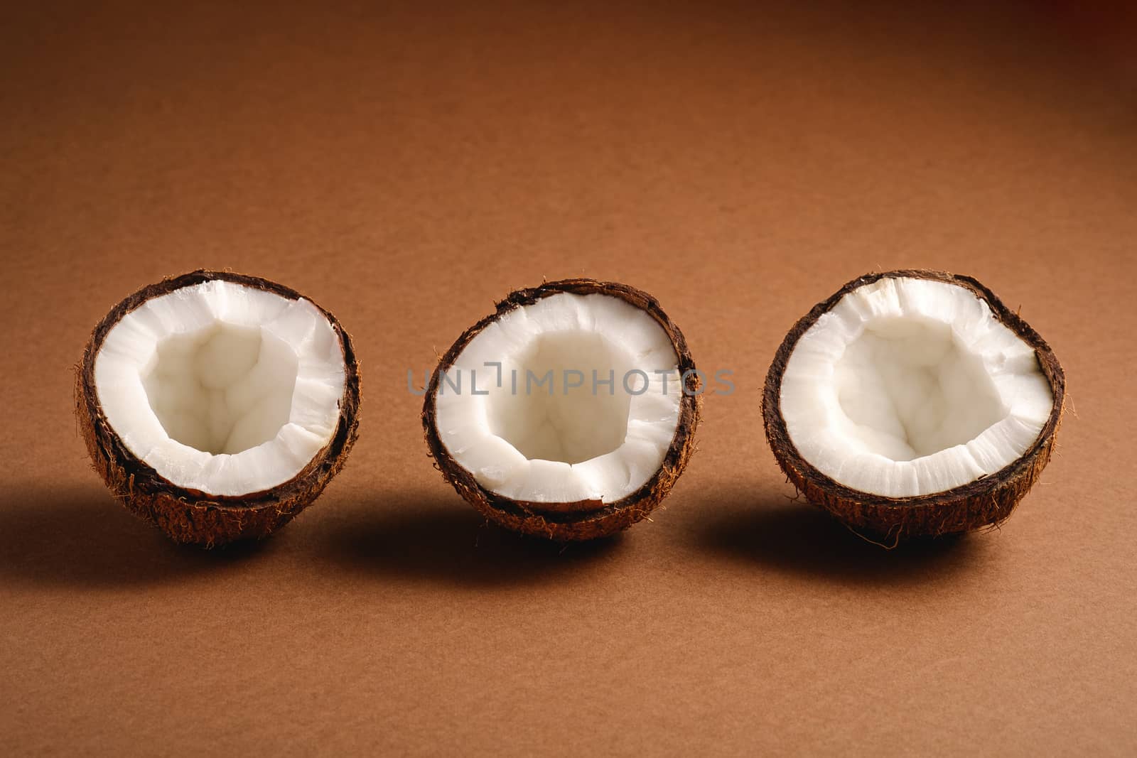 Three coconut fruits in row on brown plain background, abstract food tropical concept, angle view