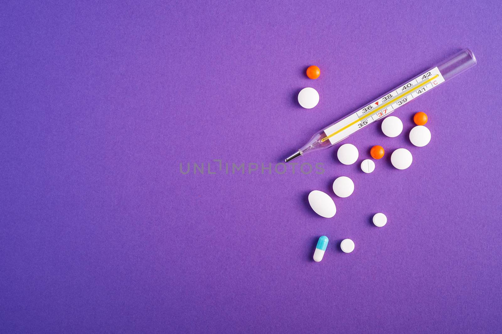 Pills, tablets and analog thermometer on violet purple background, healthcare medical concept, antibiotics and cure, top view copy space