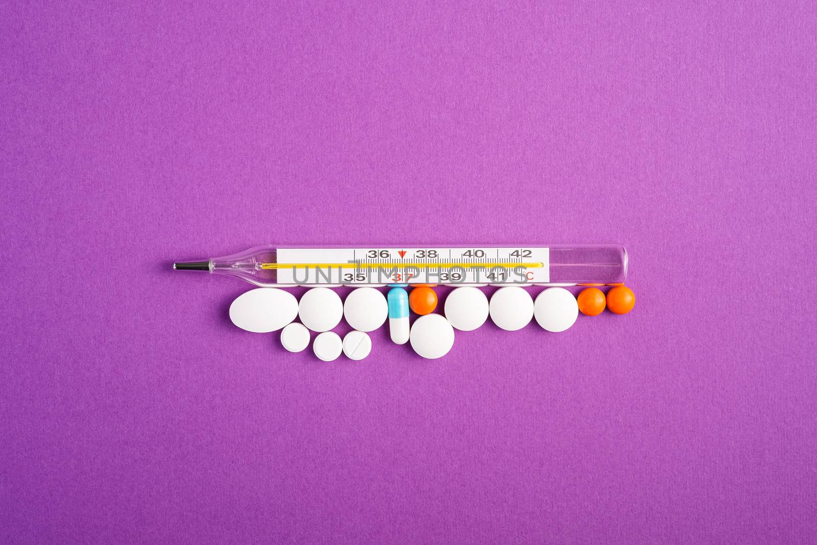 Pills, tablets and analog thermometer on violet purple background, healthcare medical concept, antibiotics and cure, top view