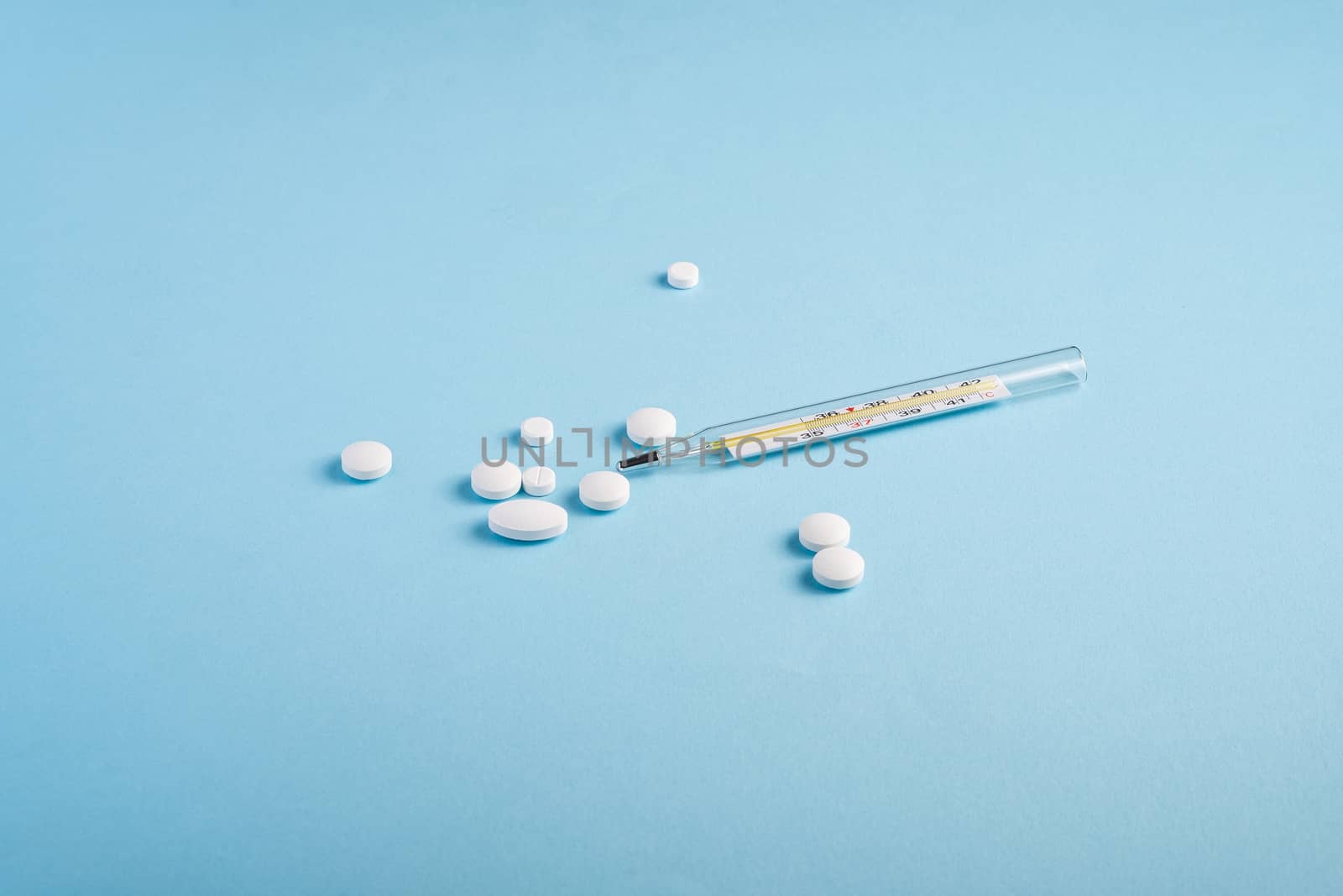 Pills, tablets and analog thermometer on bright blue background, healthcare medical concept, antibiotics and cure, angle view copy space