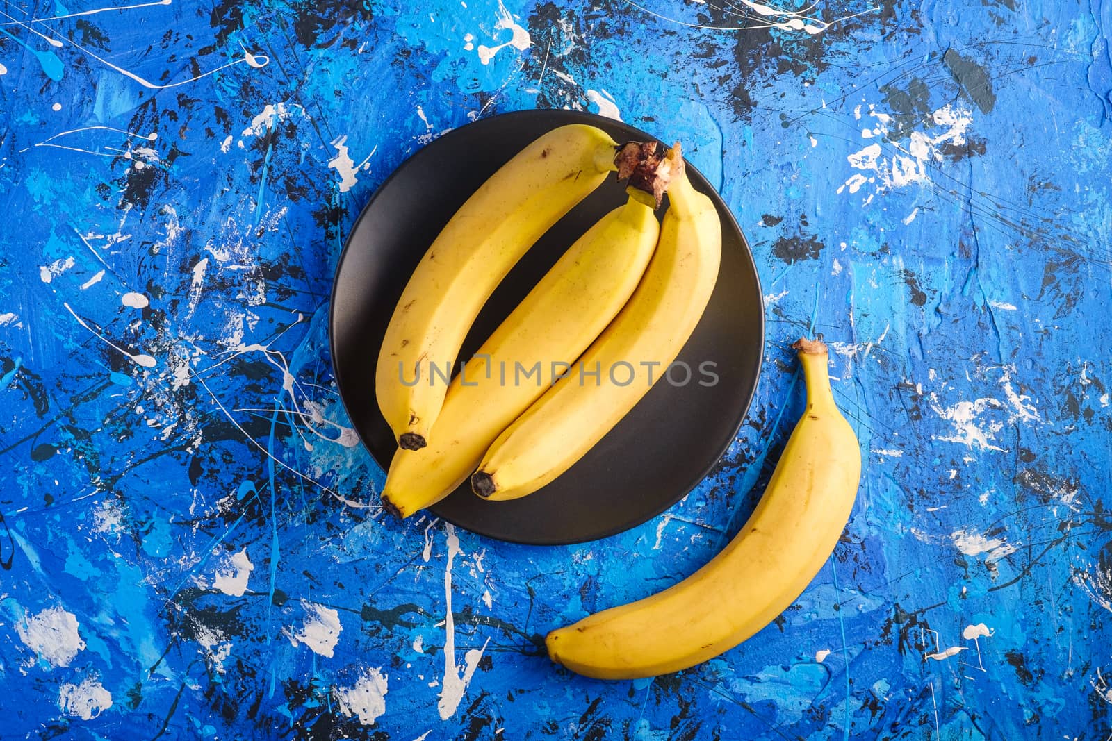 Banana fruits in black plate on blue textured background, top view copy space