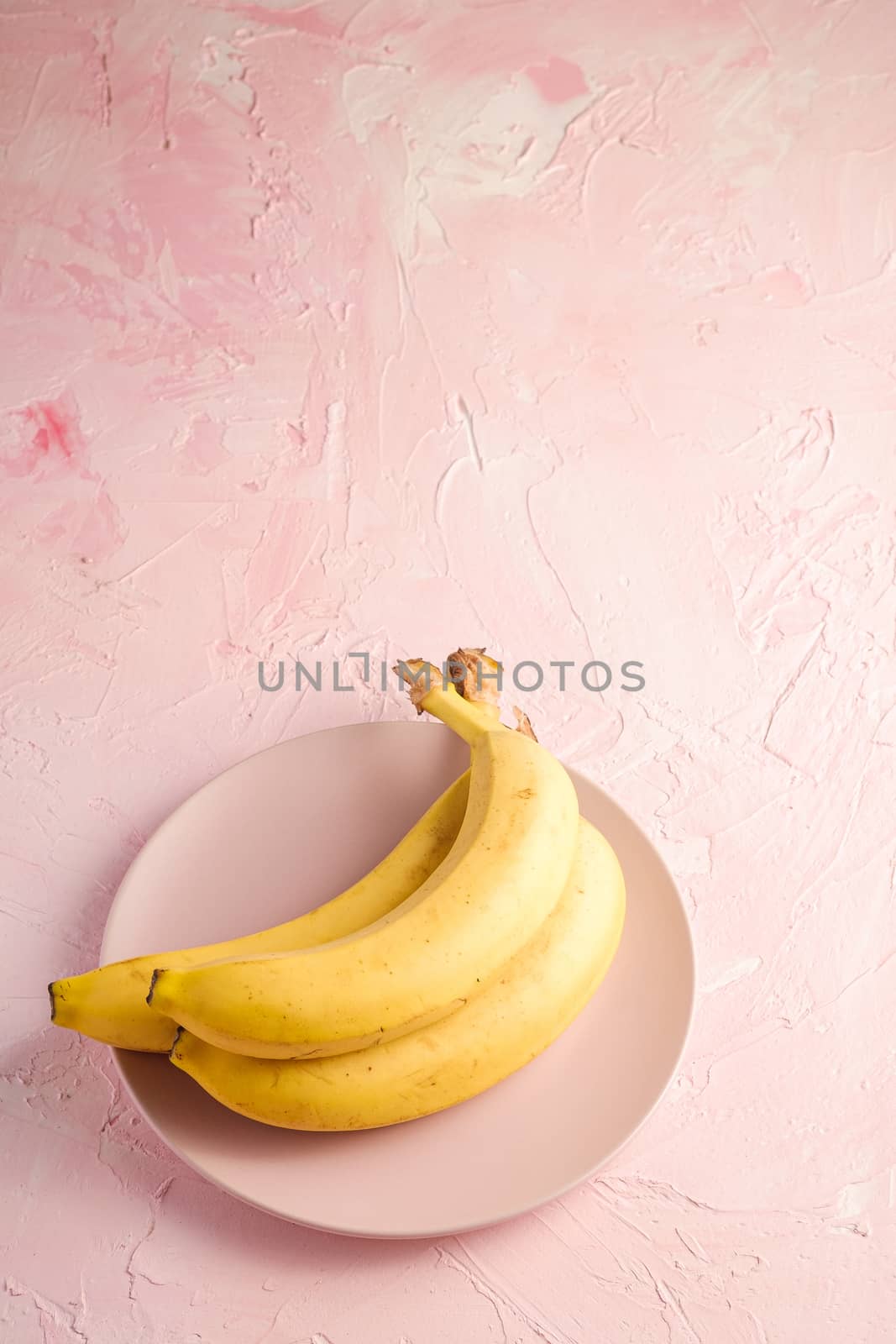 Banana fruits in pink plate on pink textured background, angle view copy space