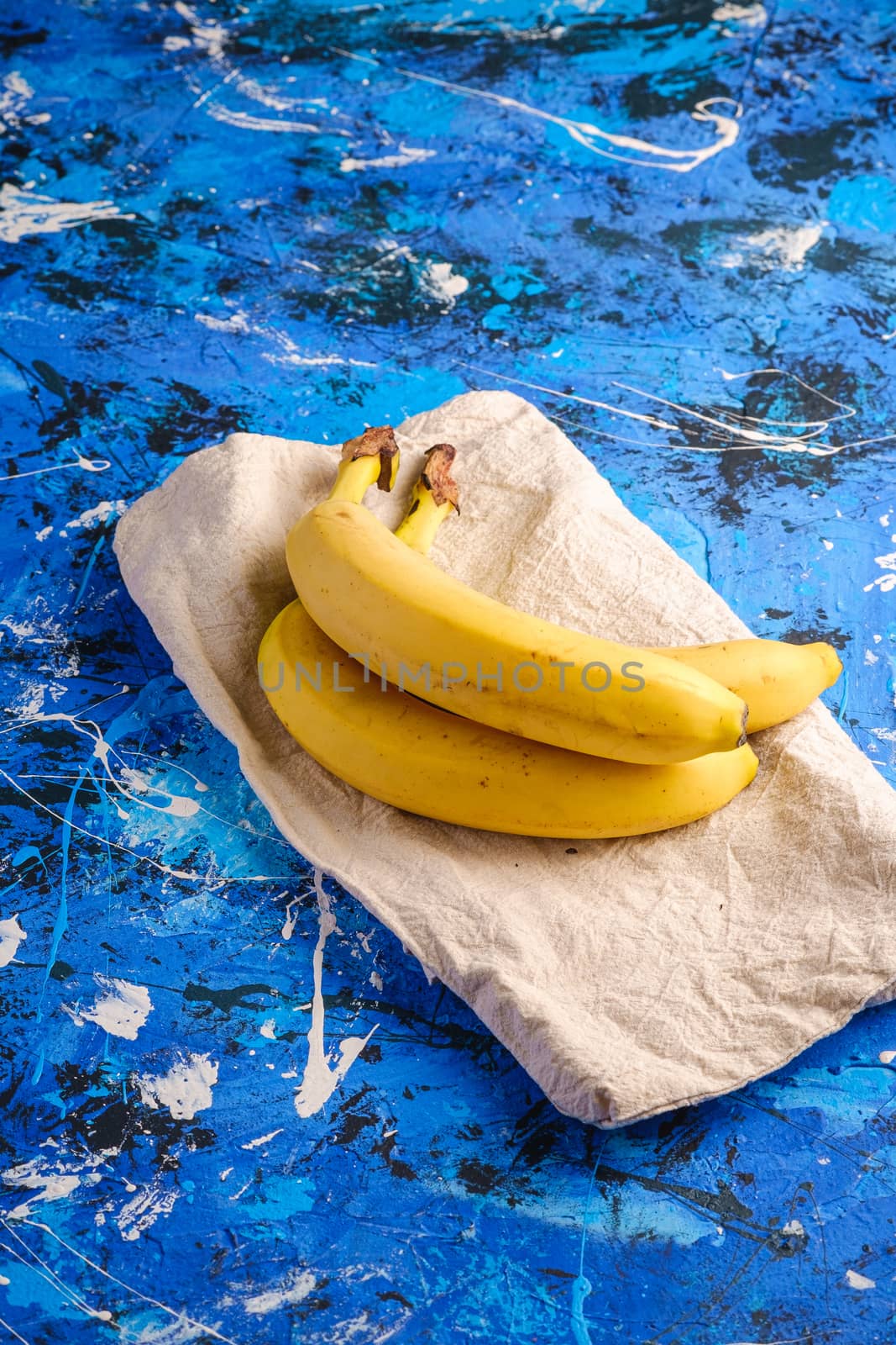 Banana fruits with tablecloth on blue textured background, angle view copy space