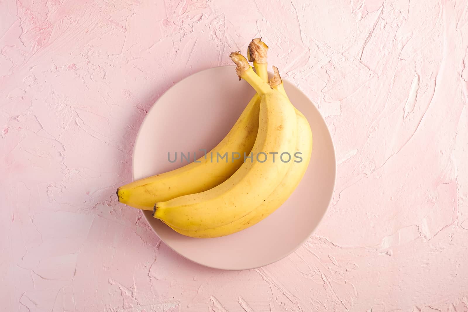 Banana fruits in pink plate on pink textured background, top view copy space