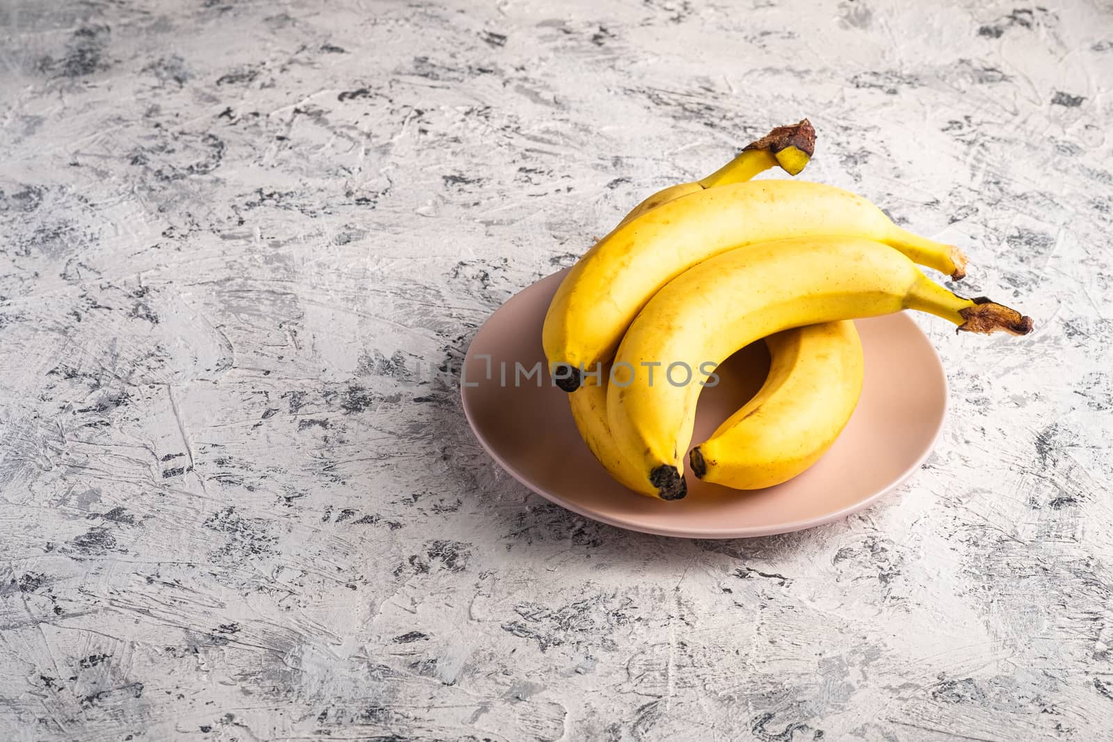 Banana fruits in pink plate on white textured background, angle view copy space