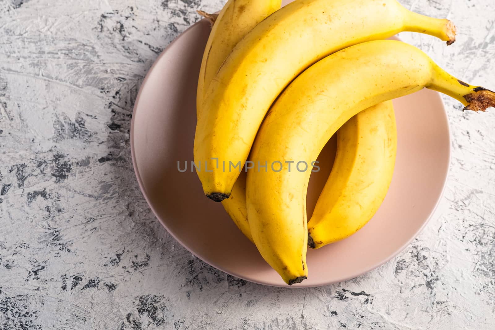 Banana fruits in pink plate on white textured background, top view copy space