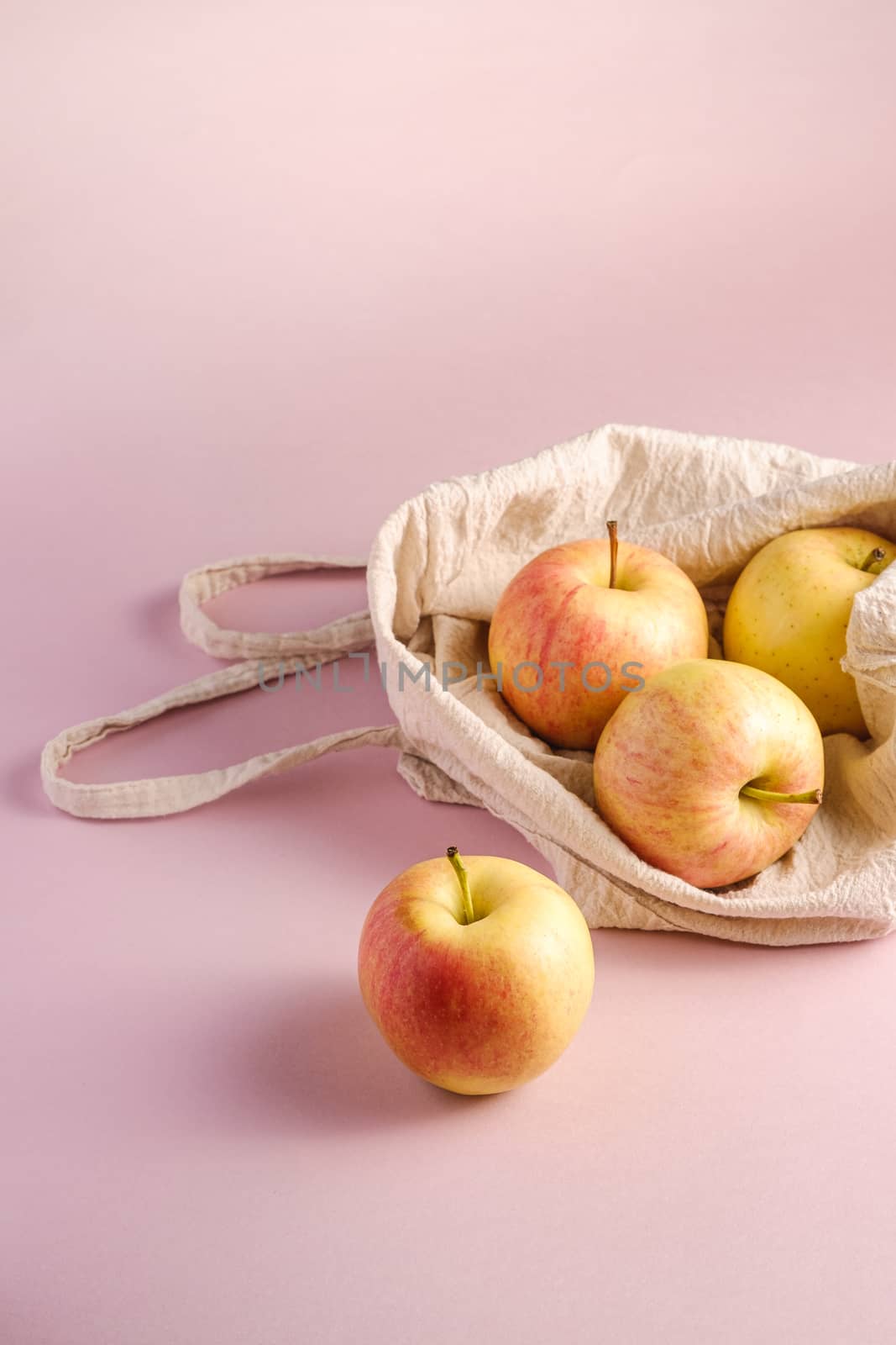 Fresh sweet apples in reusable textile grocery bag on pink background, angle view