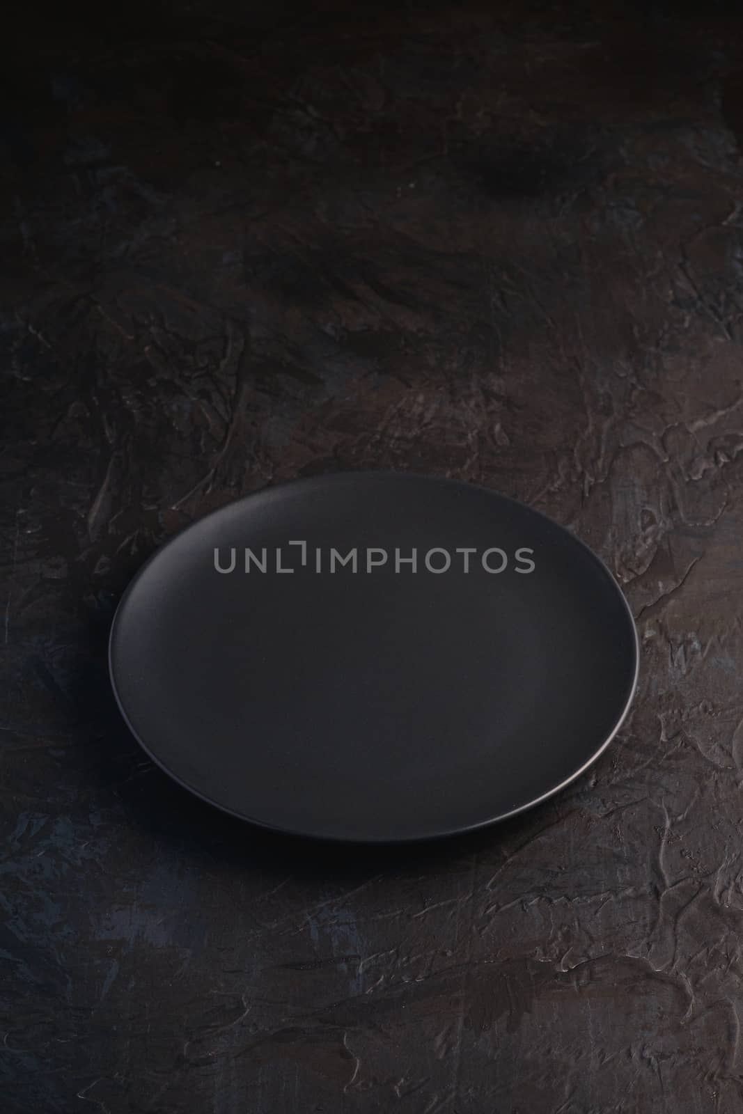 Empty black plate on dark textured background, angle view