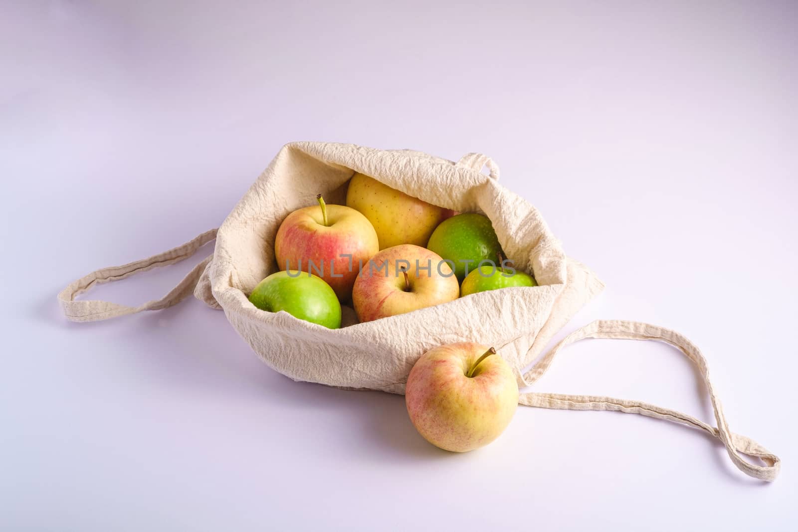 Fresh sweet apples in reusable textile grocery bag on white background, angle view