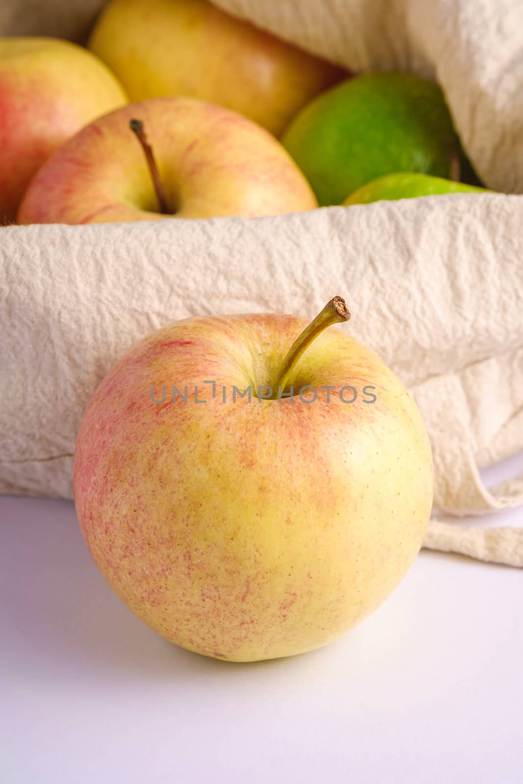 Fresh sweet apples in reusable textile grocery bag on white background, angle view macro