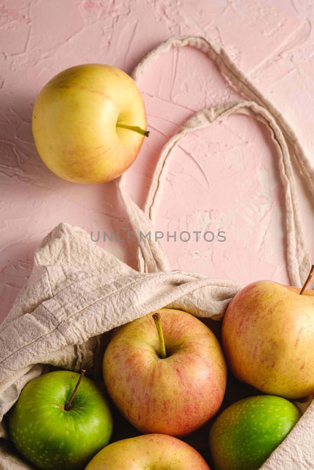 Fresh sweet apples in reusable textile grocery bag on pink textured background, selective focus