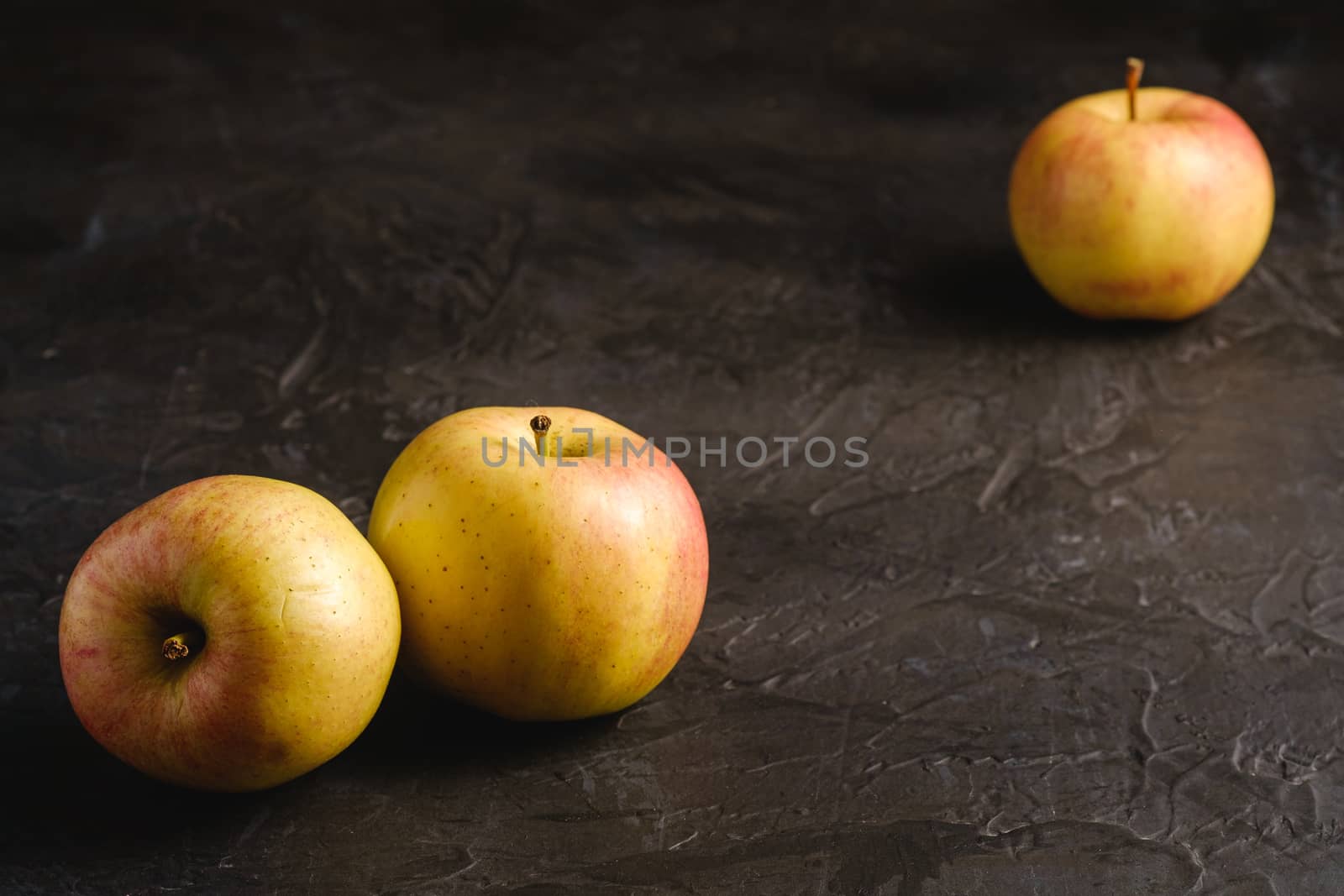 Fresh sweet three apples on dark black textured background, angle view, selective focus
