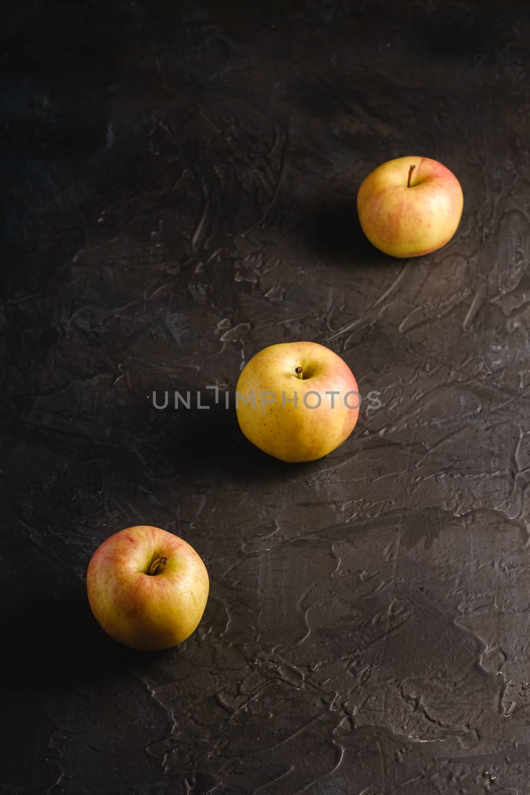 Fresh sweet three apples in row on dark black textured background, angle view
