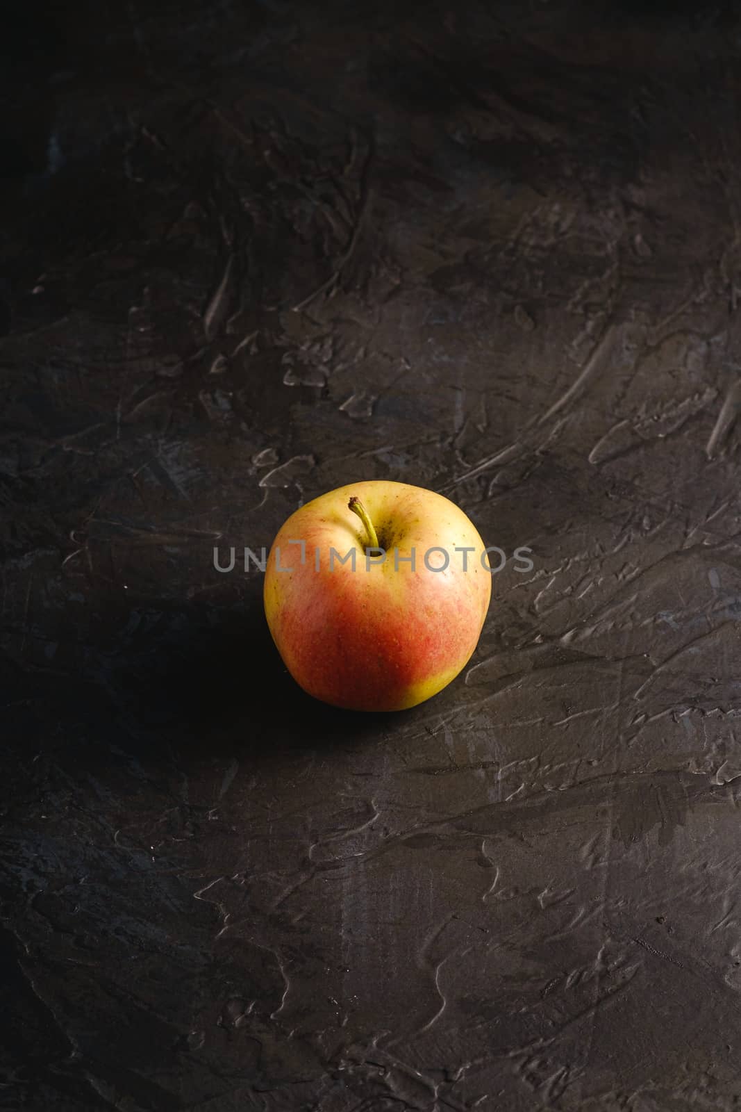 Fresh sweet single apple on dark black textured background, angle view