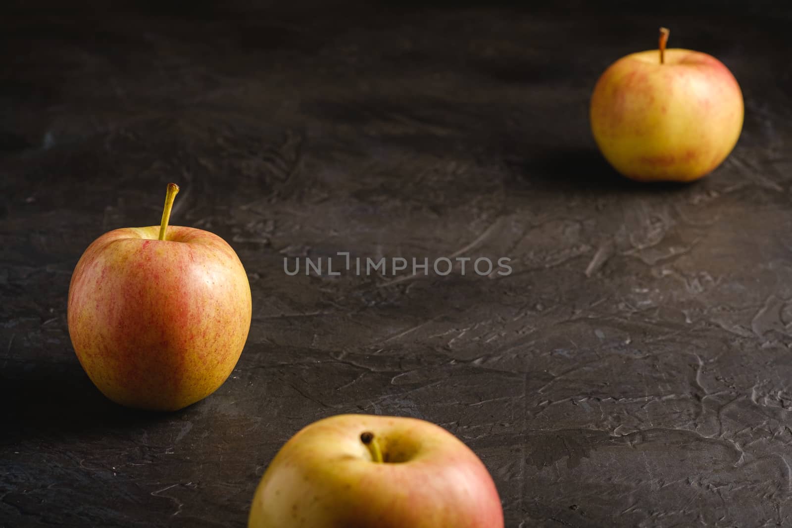 Fresh sweet three apples on dark black textured background, angle view, selective focus