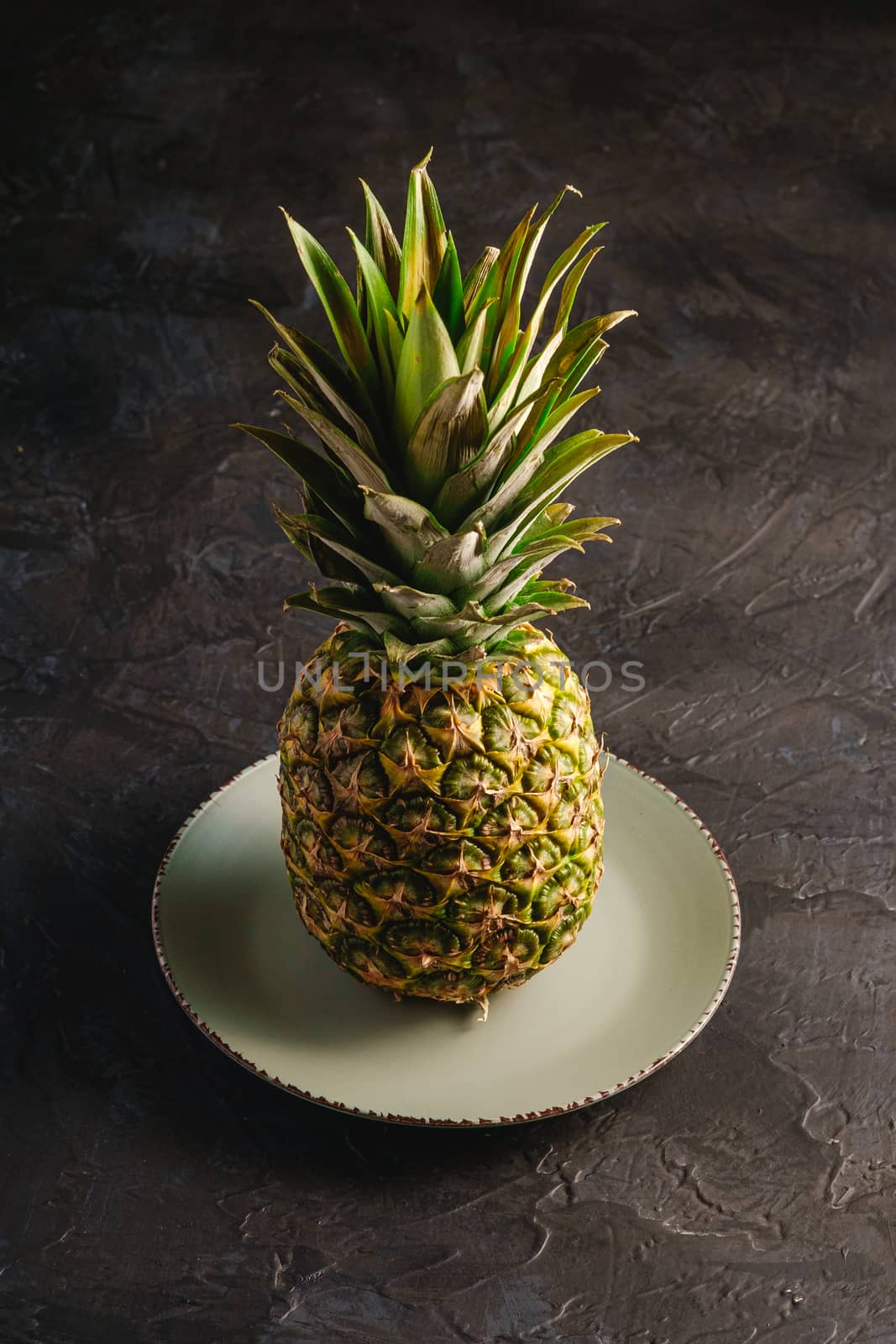 Fresh sweet pineapple in grey plate on dark black textured background, angle view