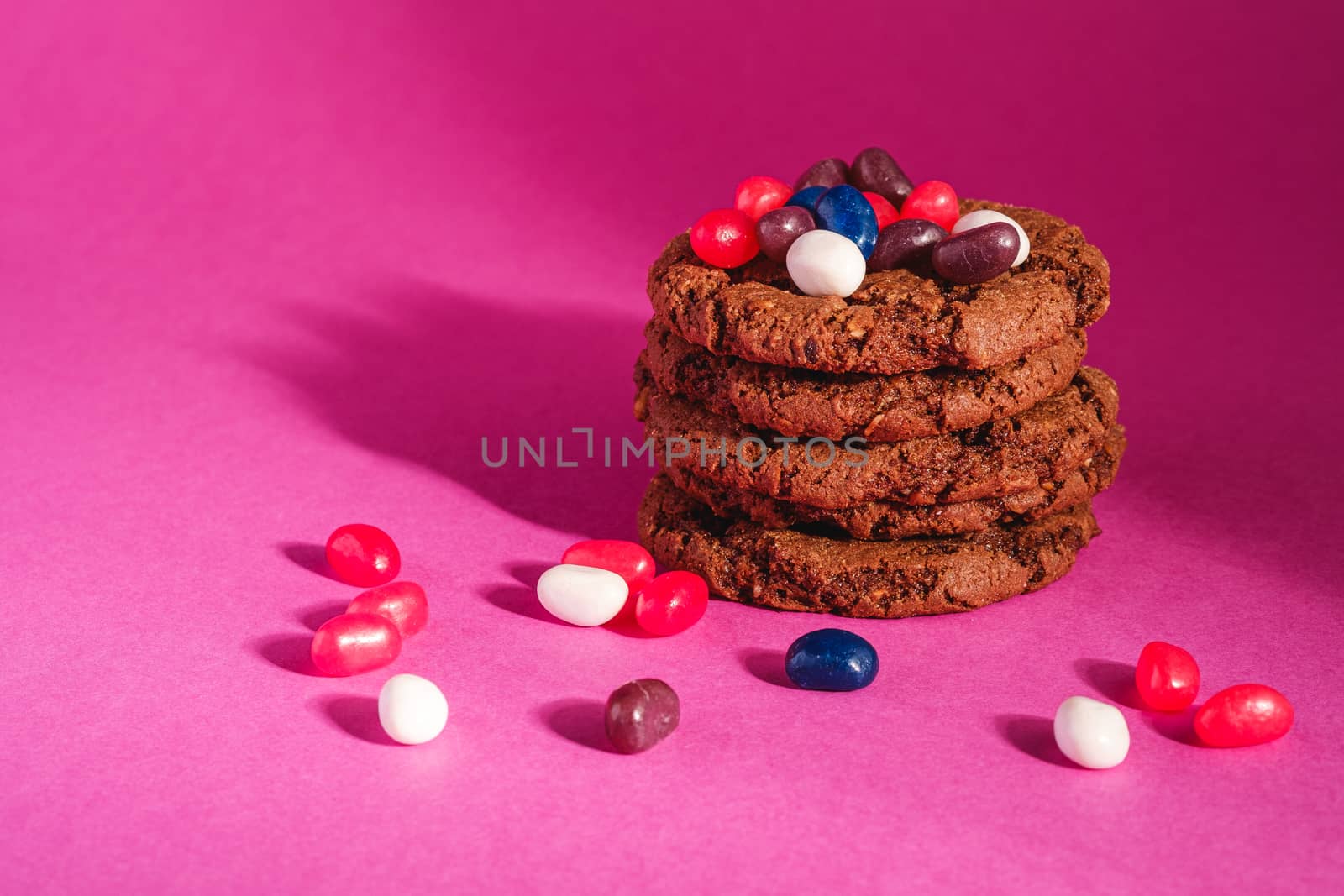 Homemade oat chocolate cookies stack with cereal with juicy jelly beans on minimal pink purple background, angle view
