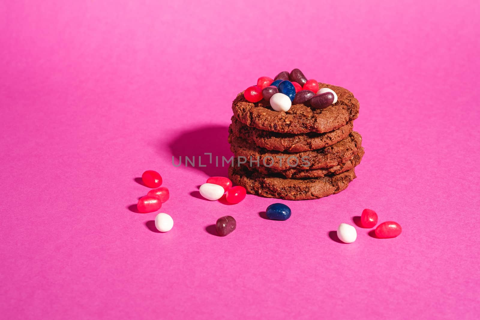 Homemade oat chocolate cookies stack with cereal with juicy jelly beans on minimal pink purple background, angle view copy space