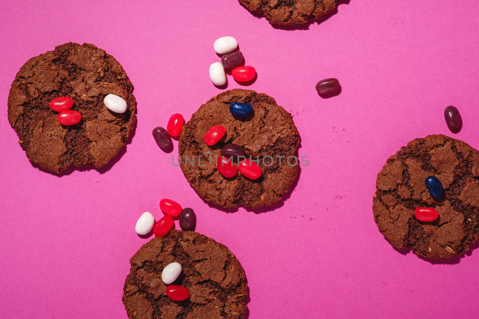 Homemade oat chocolate cookies with cereal with juicy jelly beans on minimal pink purple background, top view