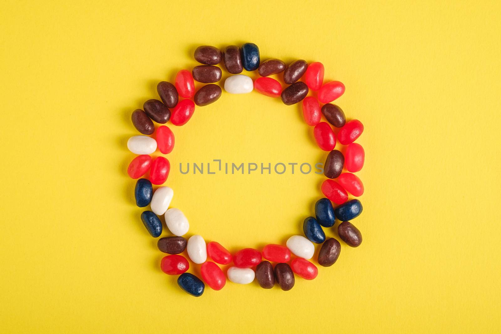 Round frame of juicy sweet fruit colorful jelly beans on bright yellow background, top view copy space