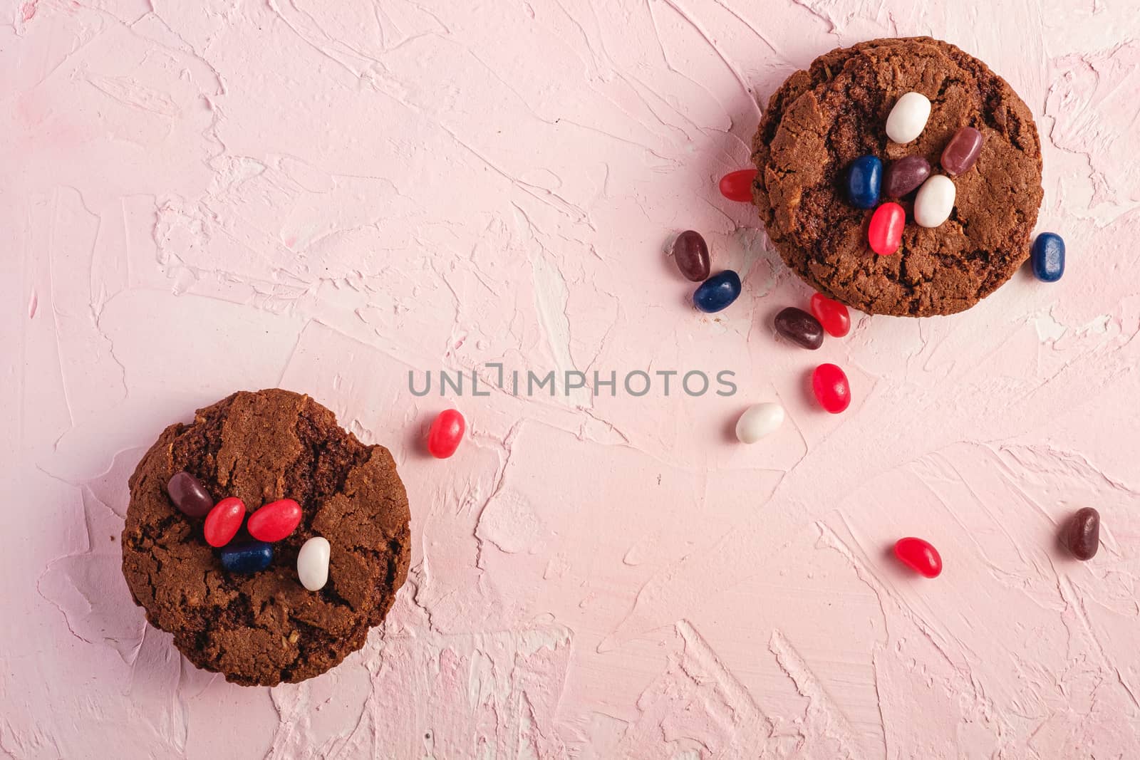 Homemade oat chocolate cookies stack with cereal with juicy jelly beans on textured pink background, top view copy space